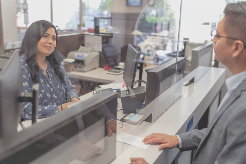 Smiling teller helping a customer illustrates Confero's customer experience research in banking industry.