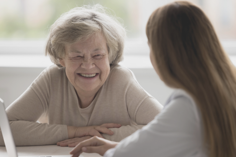 Elderly client smiling at a doctor at a desk to illustrate Confero's customer experience research in medical offices.
