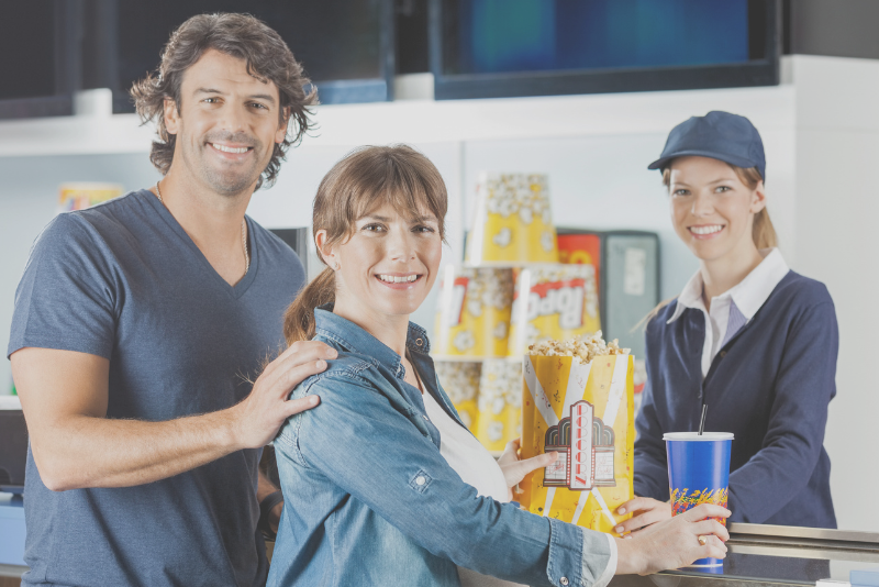 Movie theater concessions patrons smiling with a clerk to illustrate Confero's customer experience research in entertainment industry.